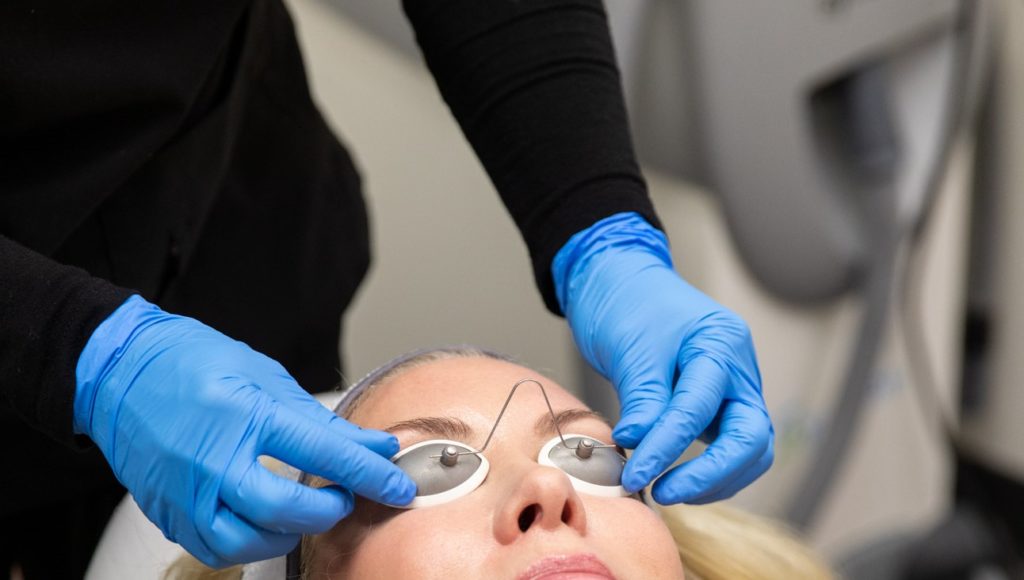 Close view of doctor placing protective eyewear on a woman's face to prepare for Forever Young BBL treatment.