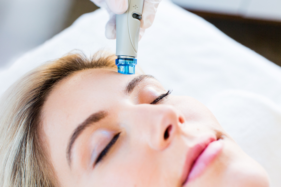 Close up of woman receiving HydraFacial MD treatment in her temple while laying down relaxed.